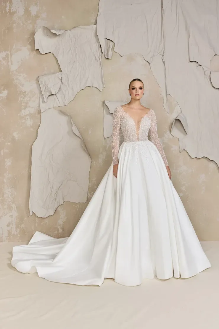 A woman in a white wedding dress is standing in front of a wall.