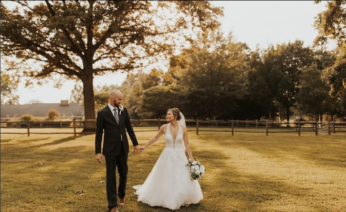A bride and groom are walking in a field holding hands.