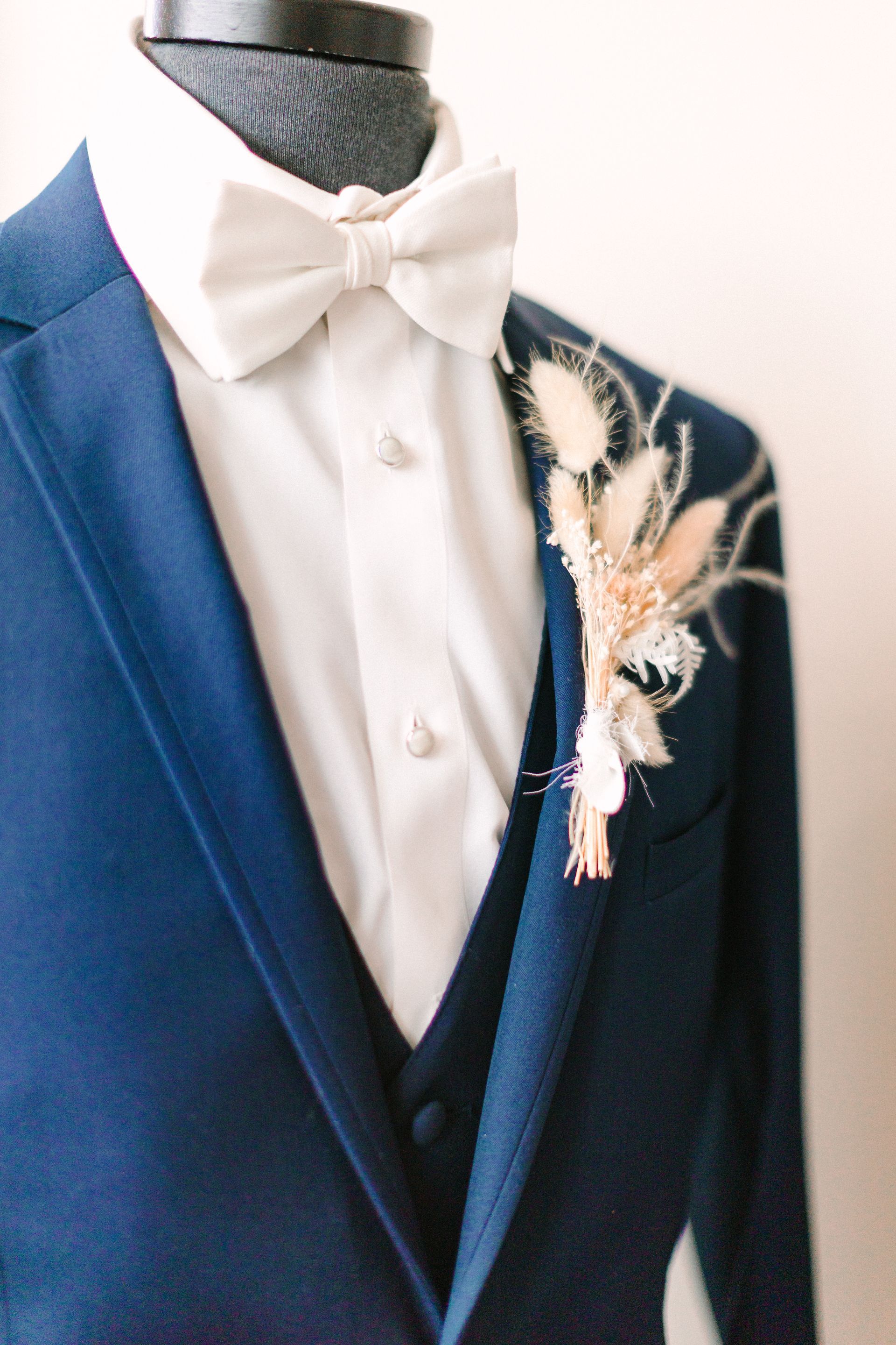 The groom is wearing a blue suit and a white bow tie.