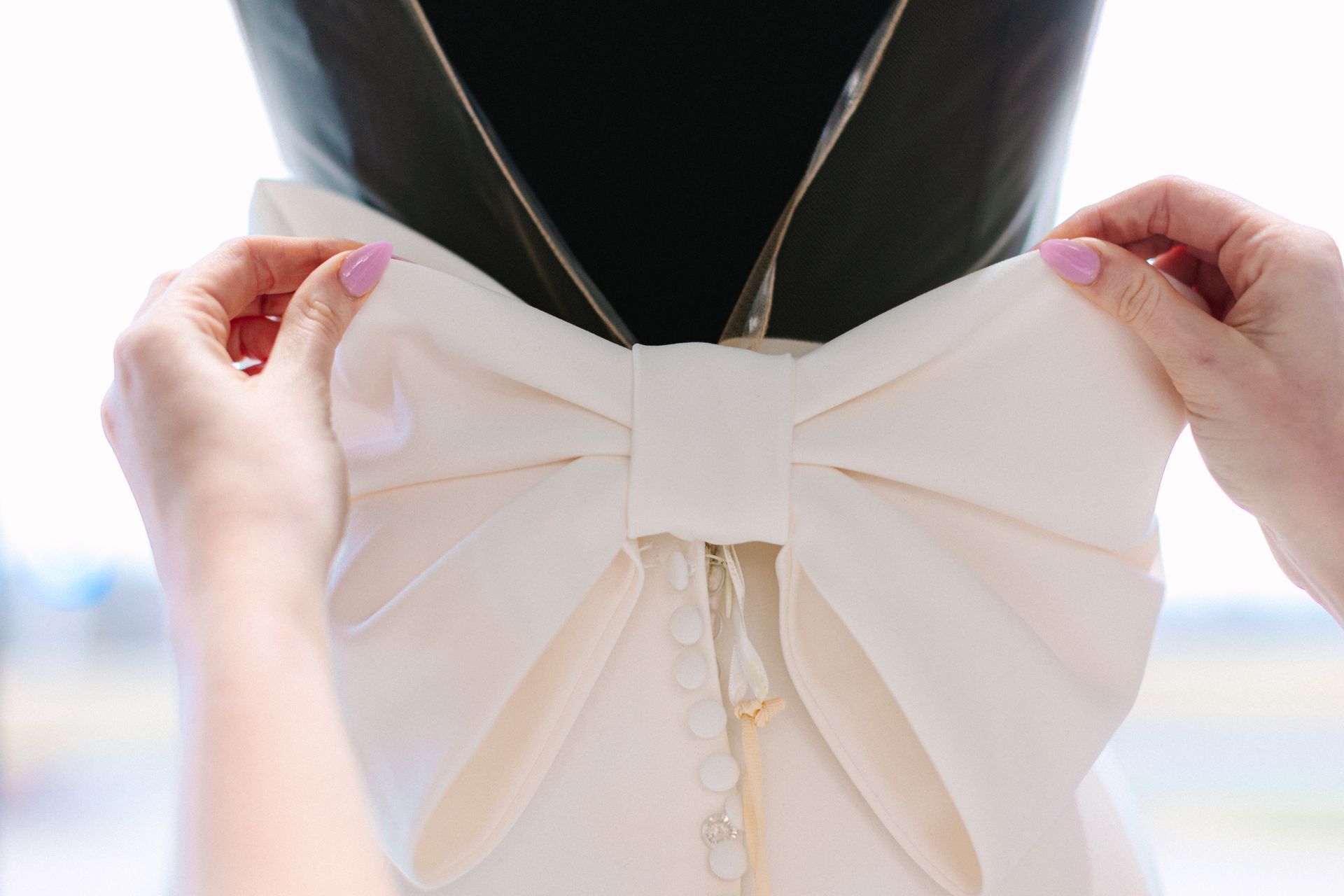A woman is tying a bow on the back of a wedding dress.