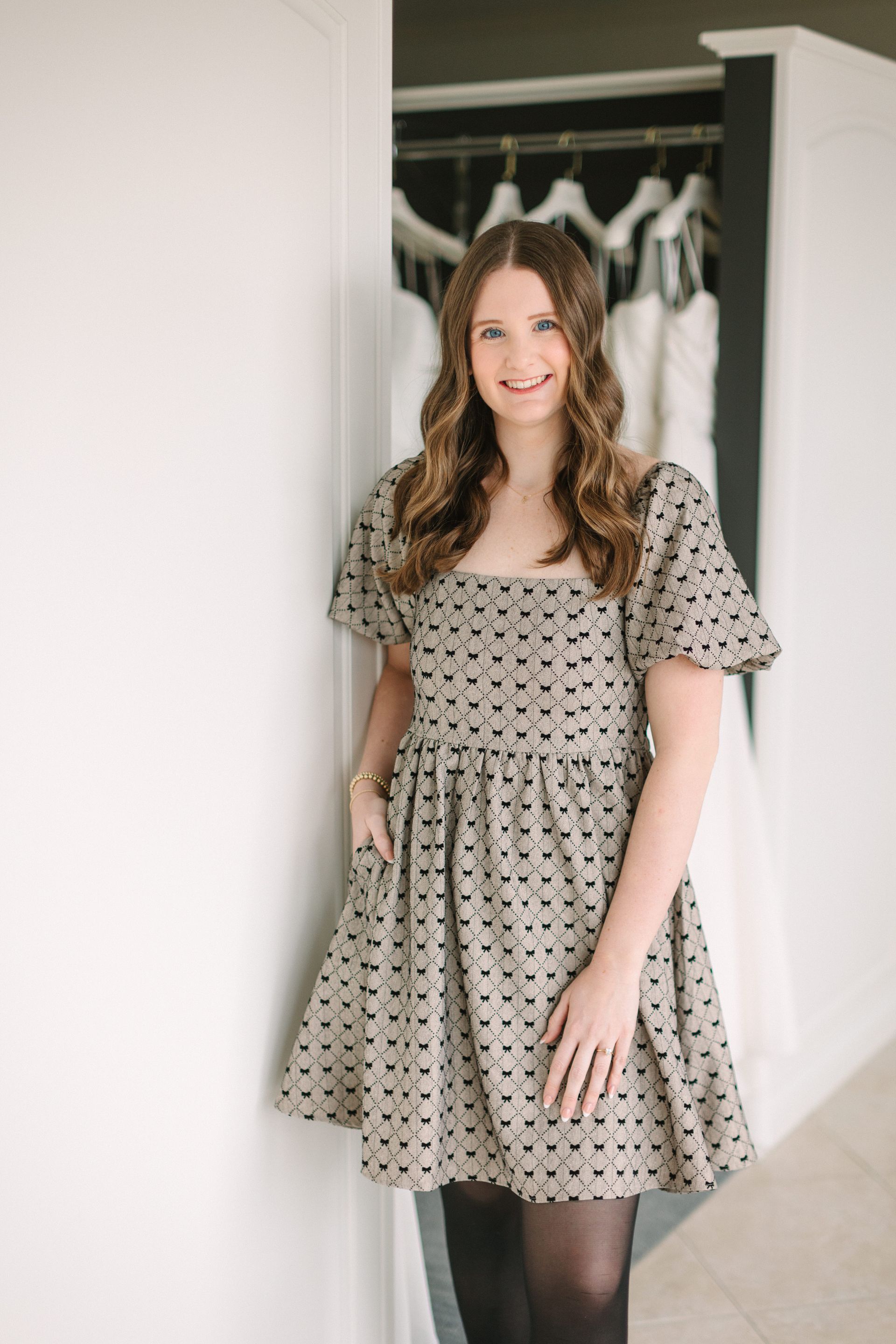 A woman in a polka dot dress and glasses is sitting on a bench.