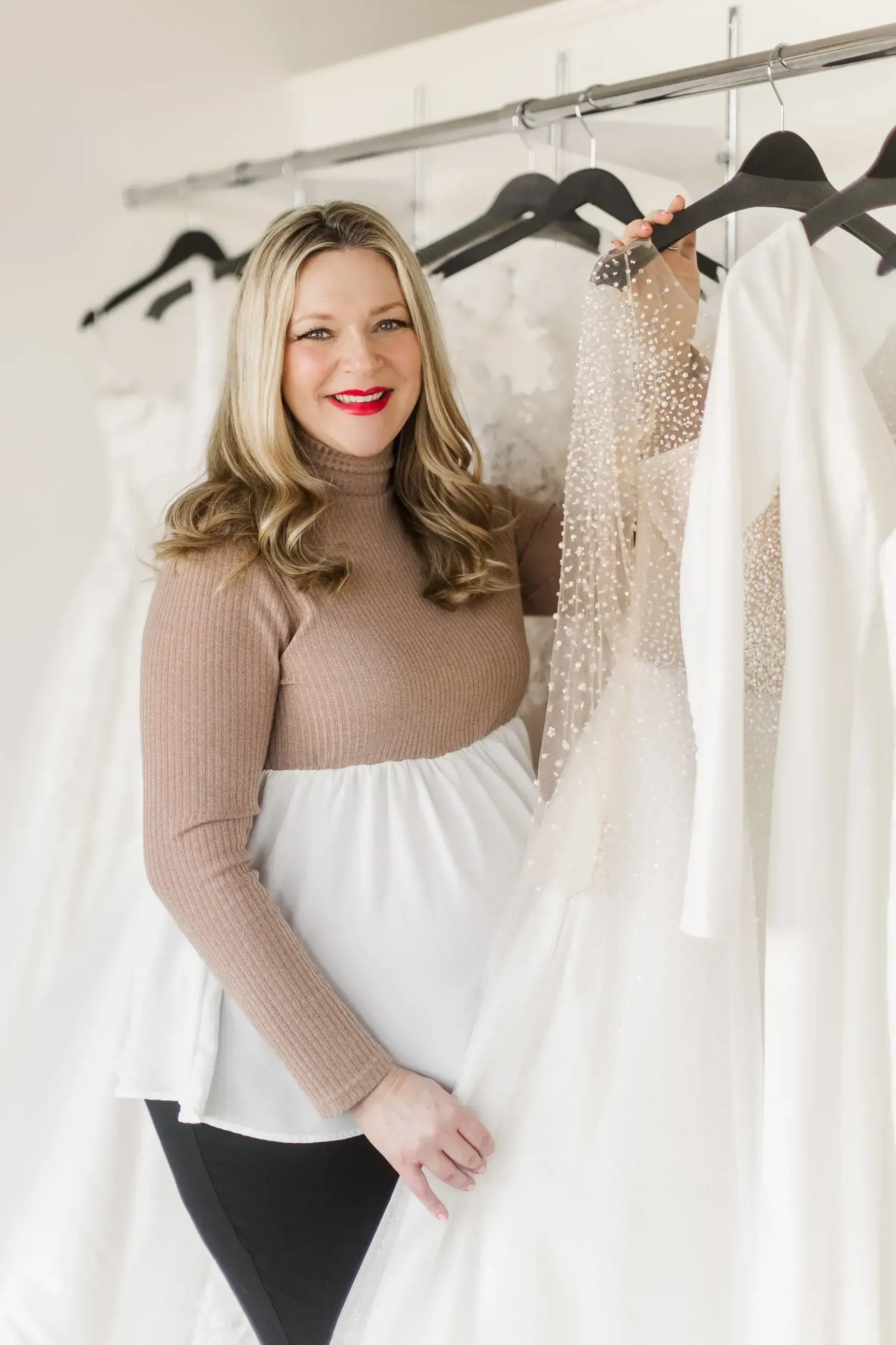 A woman is holding a wedding dress in front of a rack of wedding dresses.
