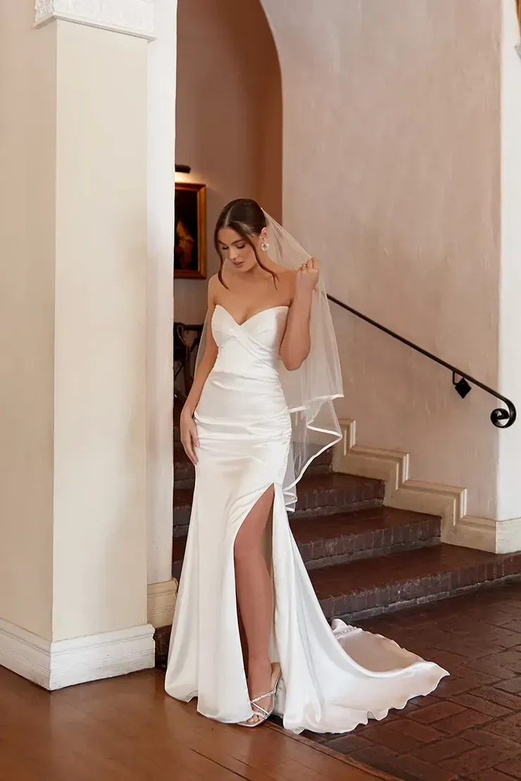 A woman in a white wedding dress and veil is standing on stairs.