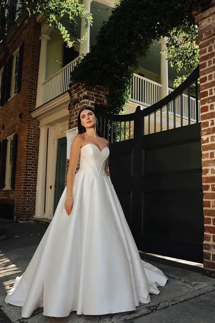 A woman in a white wedding dress is standing in front of a building.