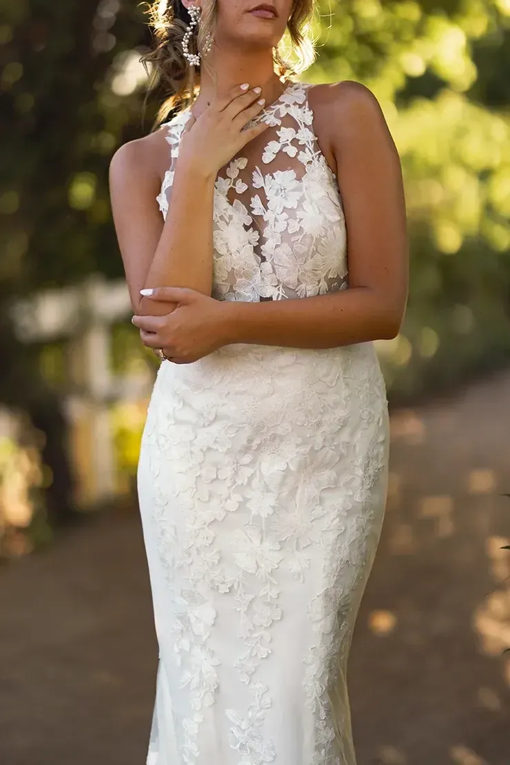 A woman in a white lace wedding dress is standing on a path.
