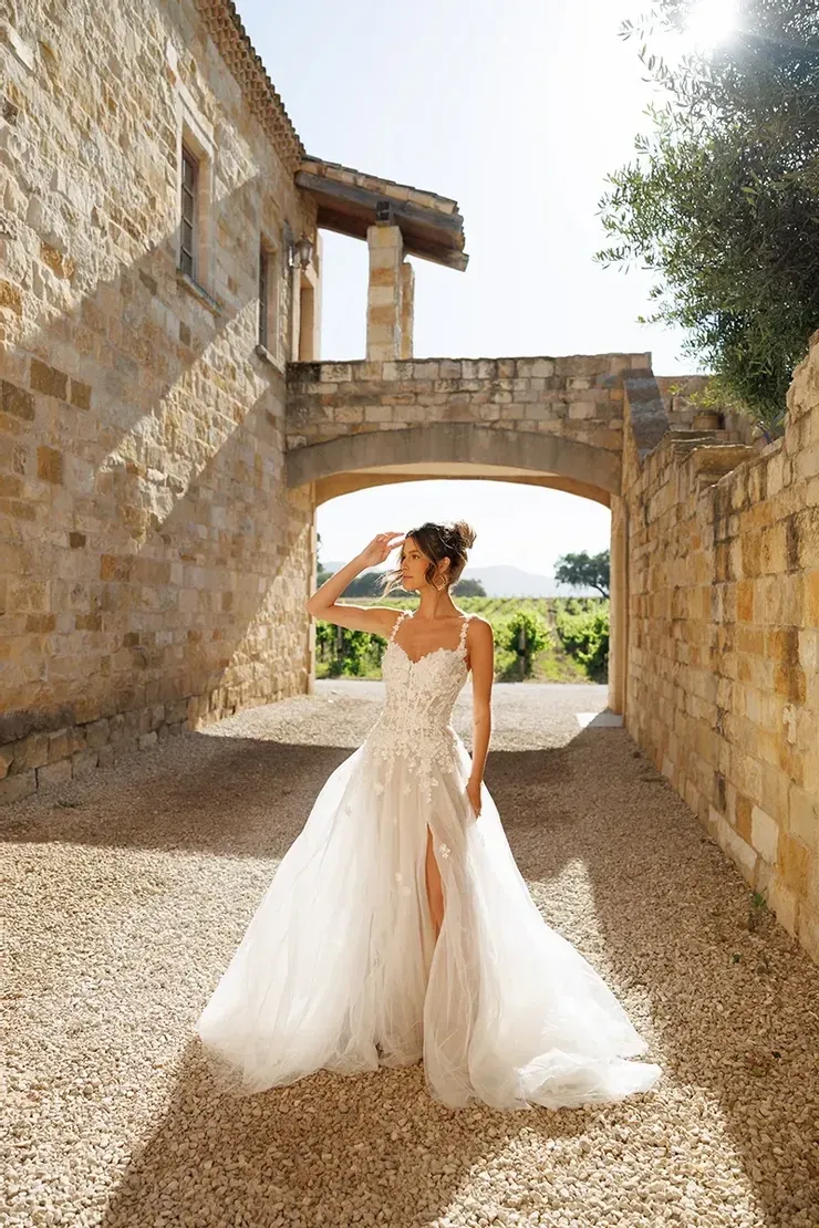 A woman in a wedding dress is standing in front of a stone building.