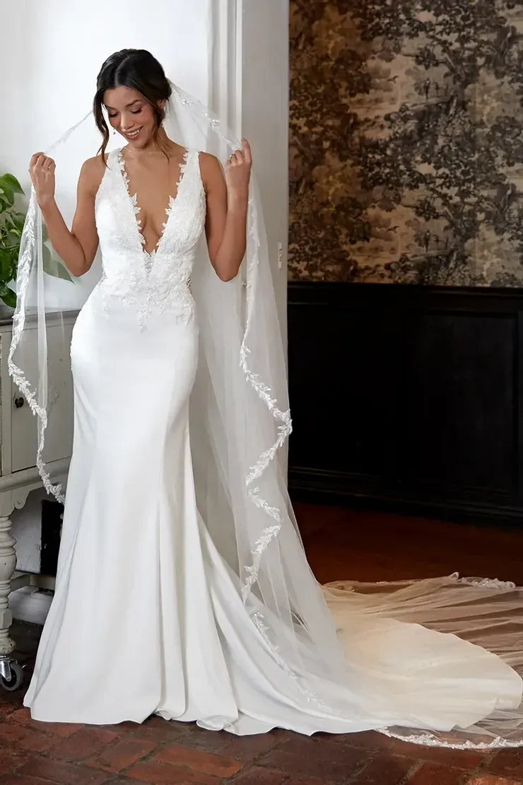A woman in a white wedding dress and veil is standing in a room.