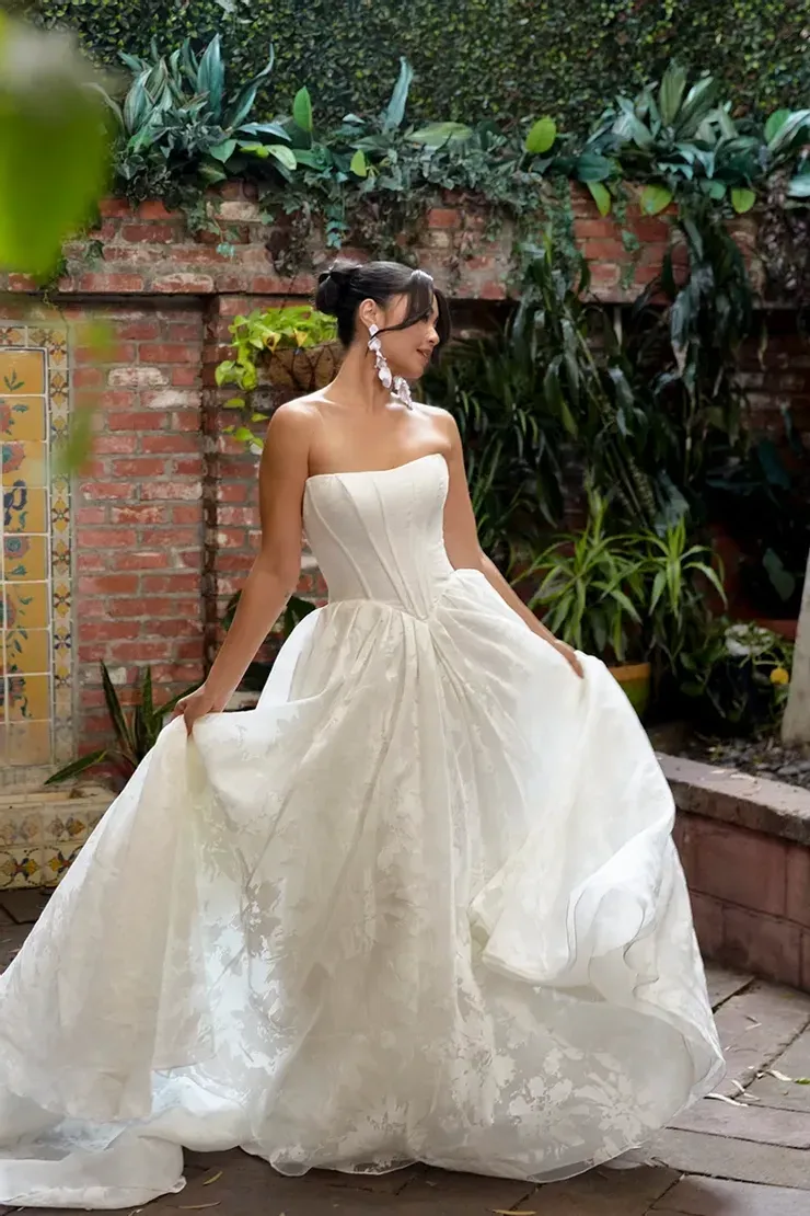 A woman in a white wedding dress is standing in front of a brick wall.