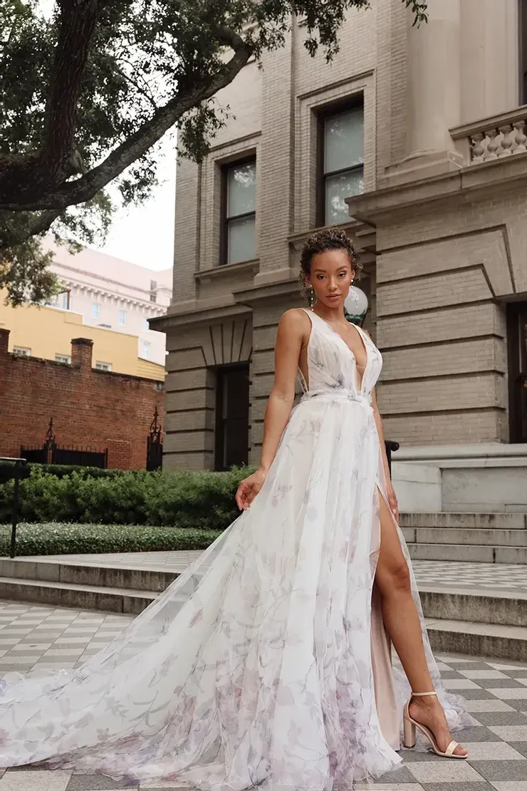 A woman in a white dress is standing in front of a building.