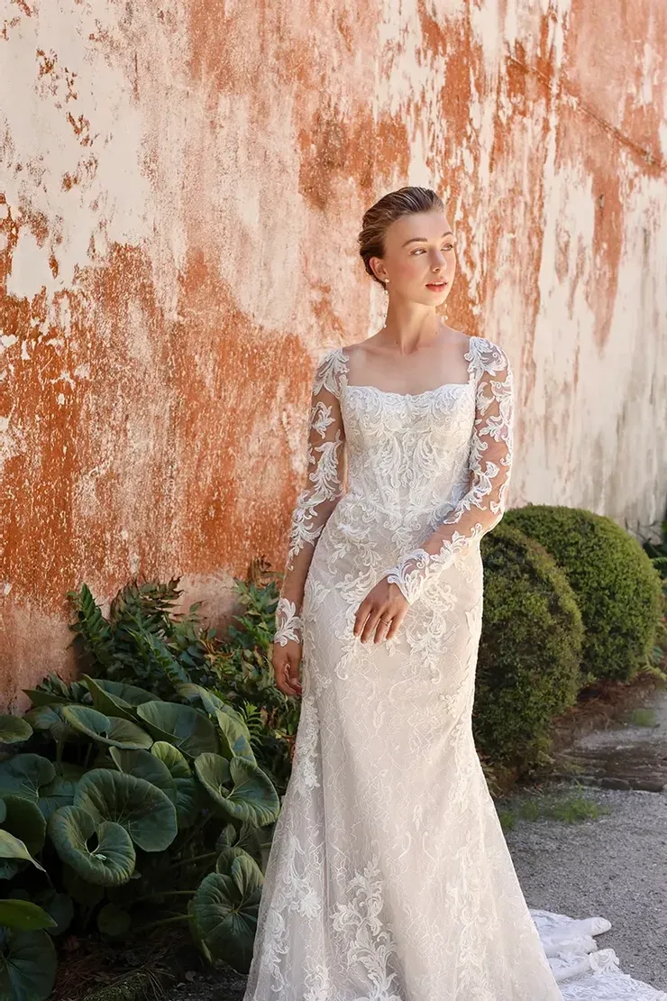 A woman in a wedding dress is standing in front of a wall.