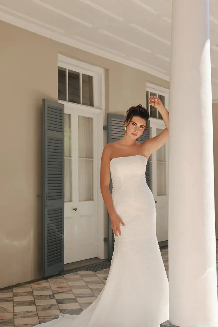 A woman in a white wedding dress is standing in front of a building.