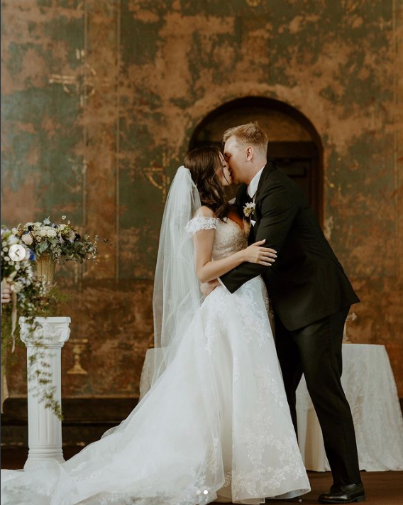 A bride and groom are kissing at their wedding ceremony.