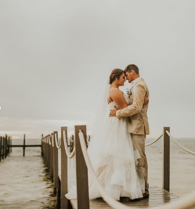 A bride and groom are hugging on a dock overlooking the ocean.