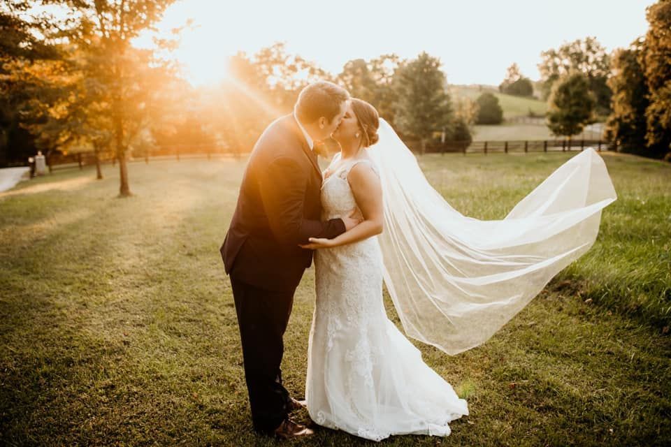 A bride and groom kissing in a field with their veil blowing in the wind.