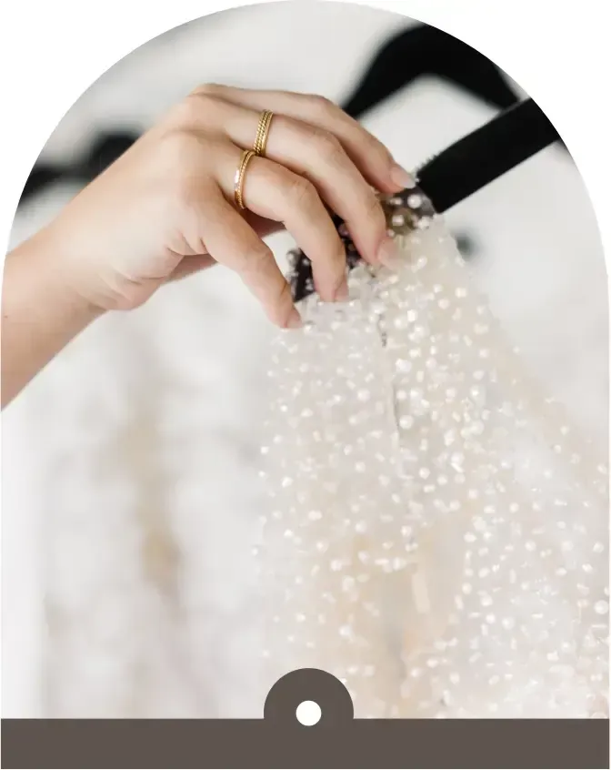 A woman 's hand is holding a white dress on a hanger.