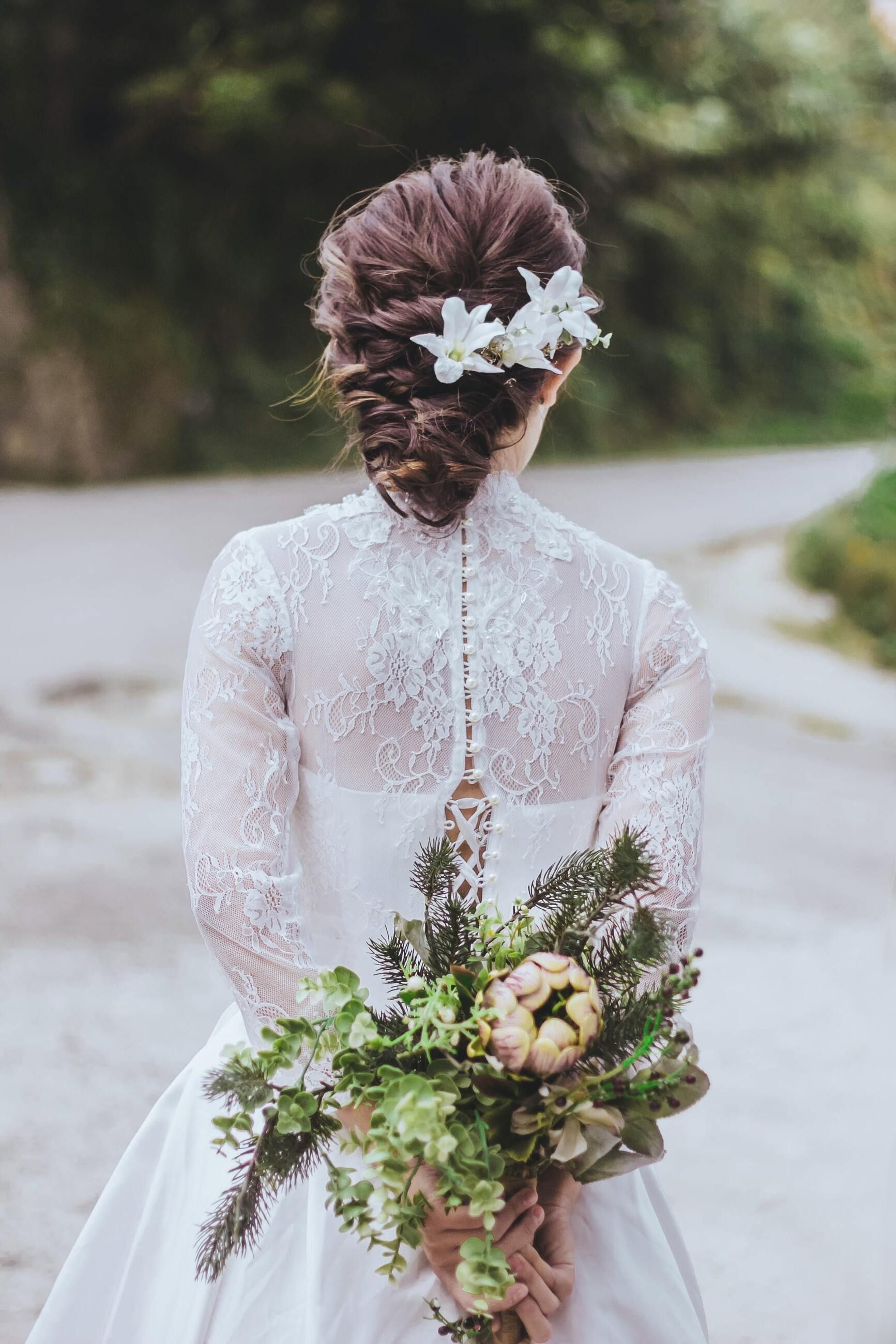 A bride in a white dress is holding a bouquet of flowers behind her back.