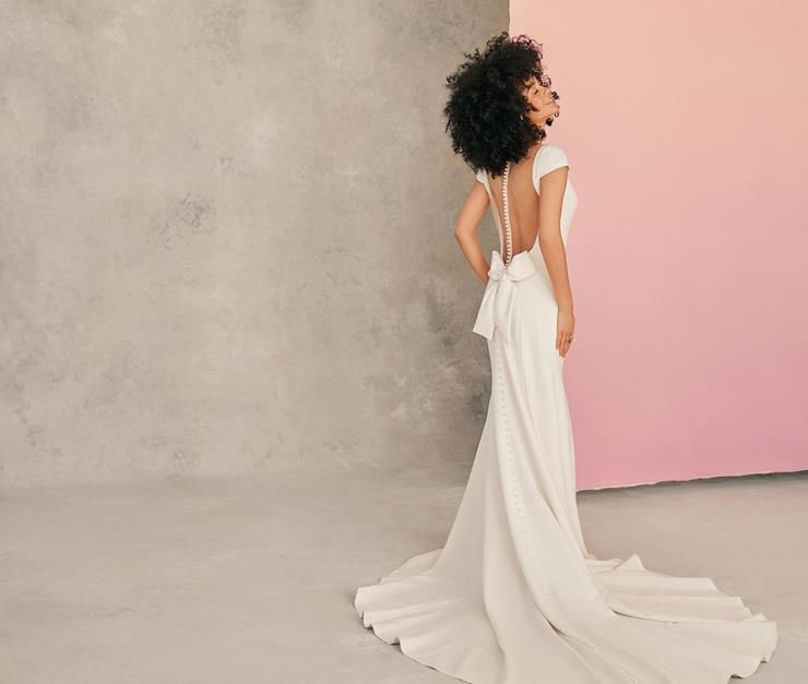 A woman in a white wedding dress is standing in front of a pink wall.