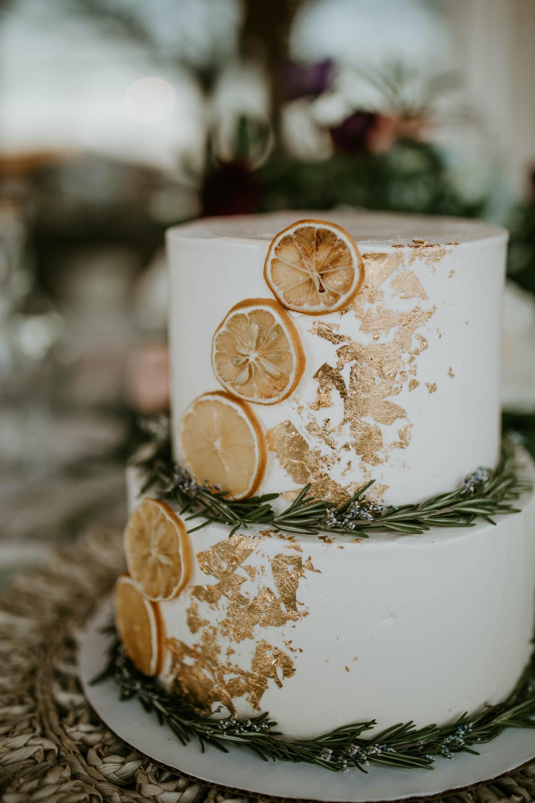 A wedding cake with lemon slices and gold leaf on it is on a table.