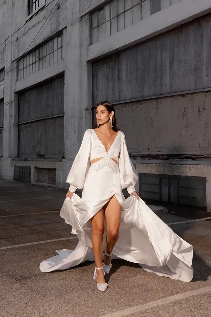 A woman in a white dress is standing in front of a building in a parking lot.