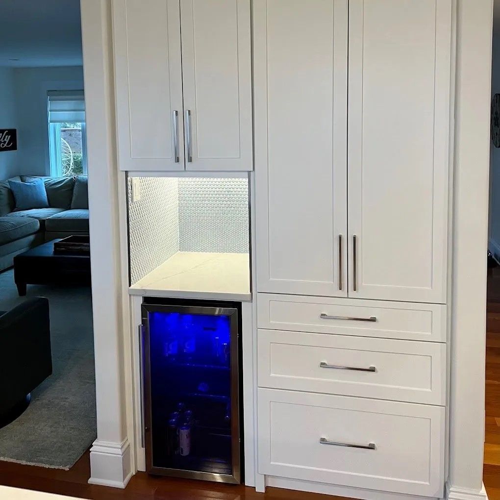 White shaker-style cabinets with a built-in mini fridge and textured backsplash in a modern kitchen refacing project. 