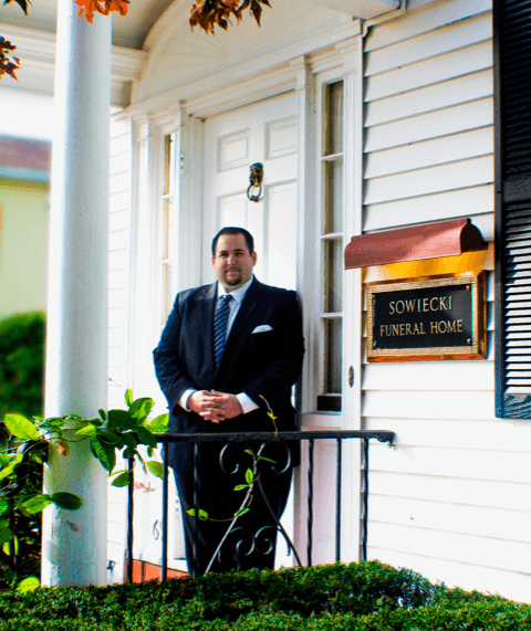 a man in a suit and tie stands in front of a funeral home