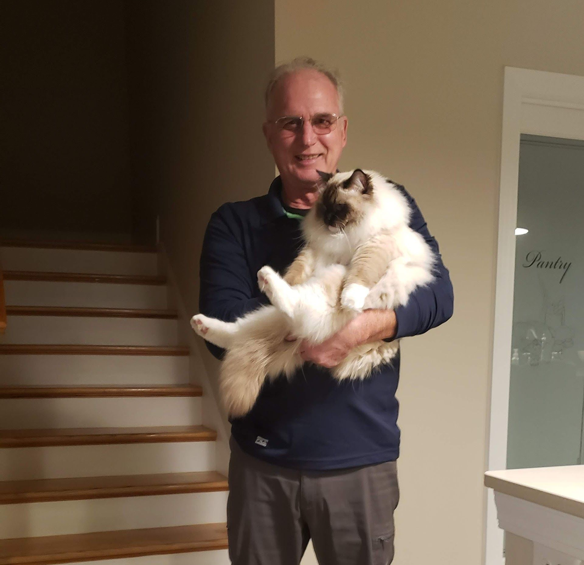 Man holding a fluffy cat indoors near a staircase and glass door