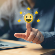 Hand tapping a glowing smiley icon above a laptop on a desk