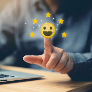 Hand tapping a glowing smiley icon above a laptop on a desk