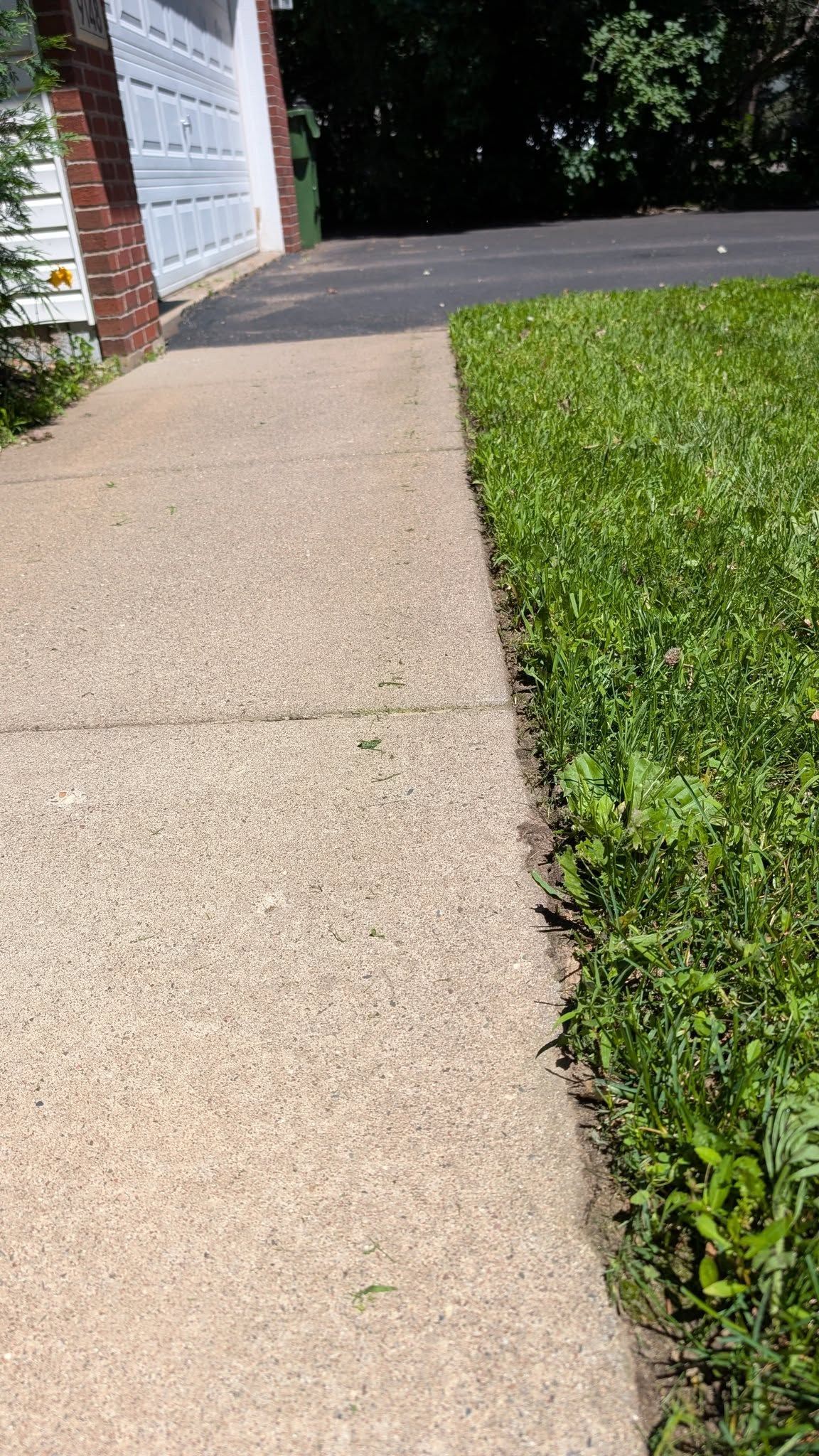 Concrete sidewalk next to green grass and a driveway leading to a garage.