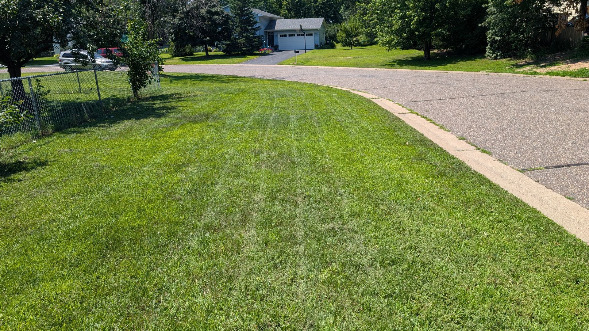Green lawn curves to meet a gravel driveway and road, sunny day.