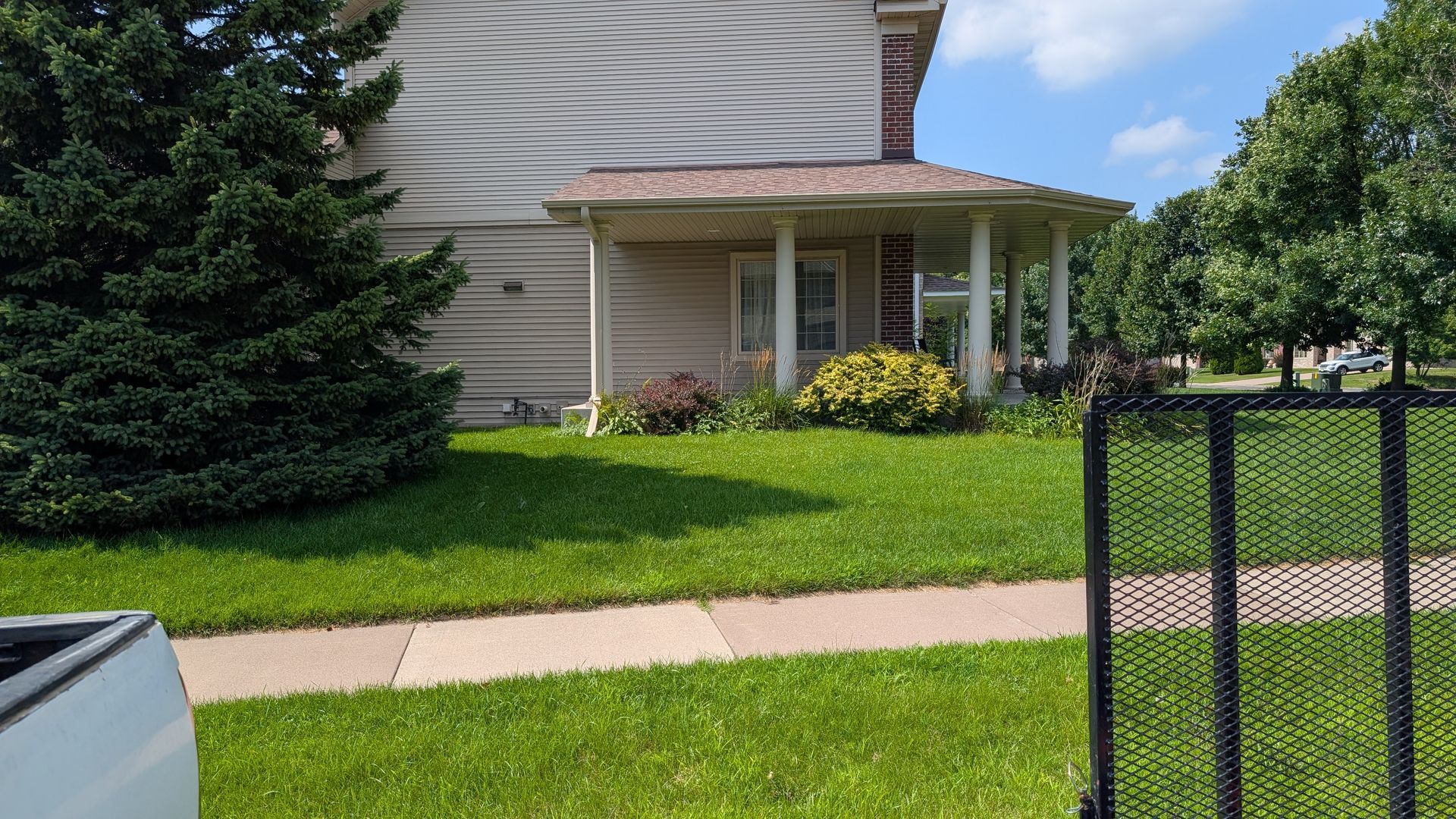 A house with a porch and green lawn under a blue sky, with some landscaping.