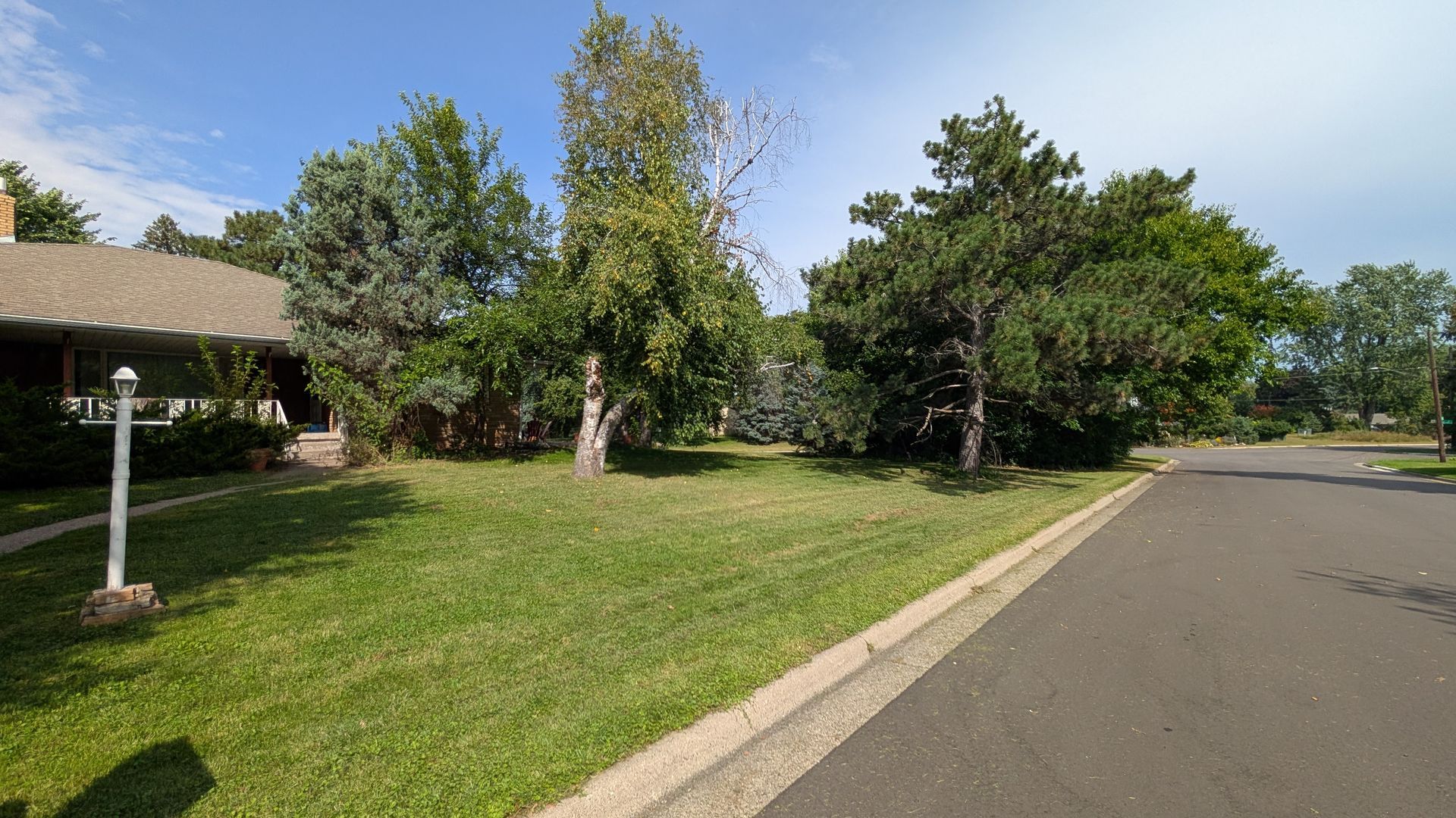 Green grass and trees flank a street next to a house on a sunny day.