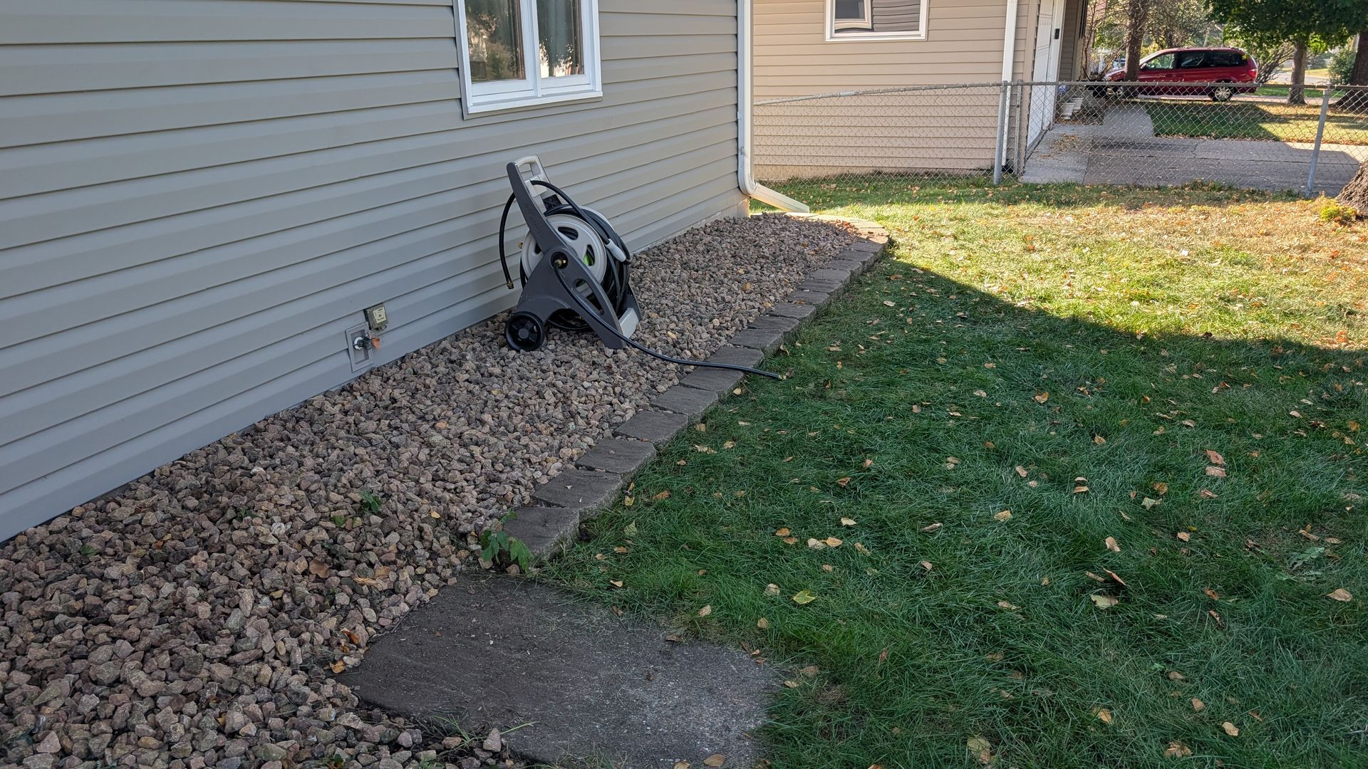 A stroller next to a house with a rock bed and concrete path.