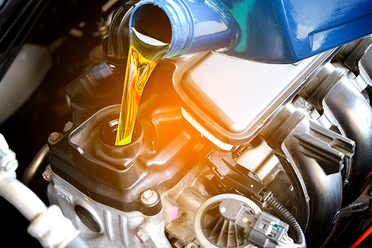A close up of a person pouring oil into a car engine.