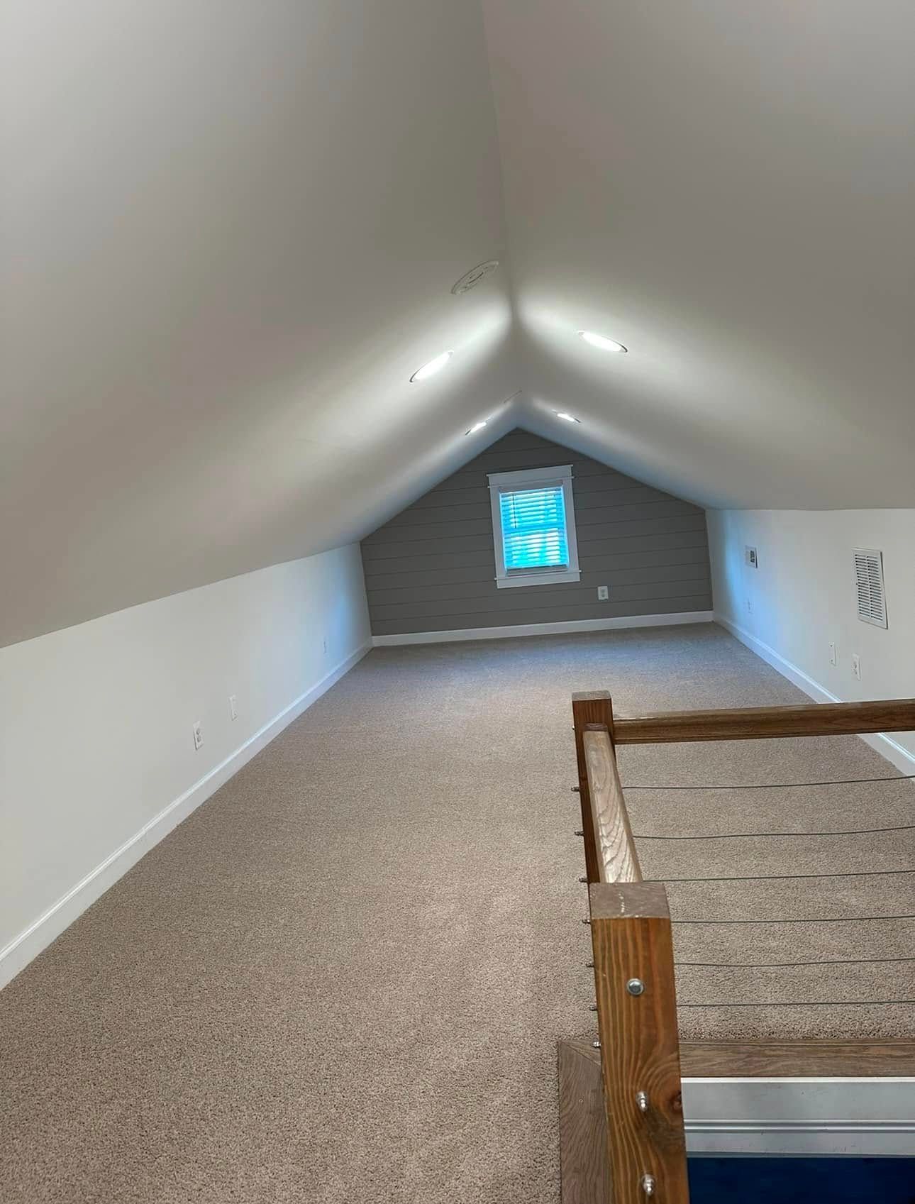 Loft interior with tan carpet, white walls, and a small window. Wooden railing on the right.