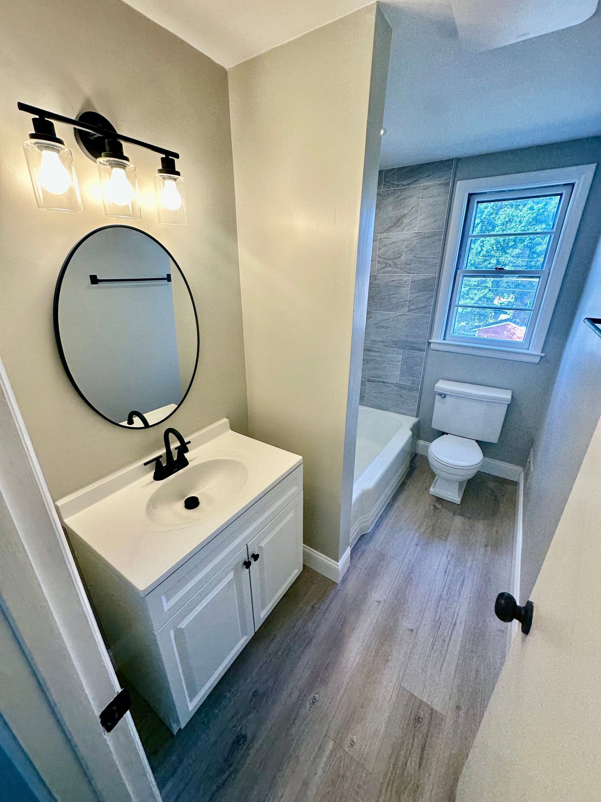 Small bathroom with a toilet, sink, mirror, and chrome fixtures. Gray walls and a decorative light fixture.