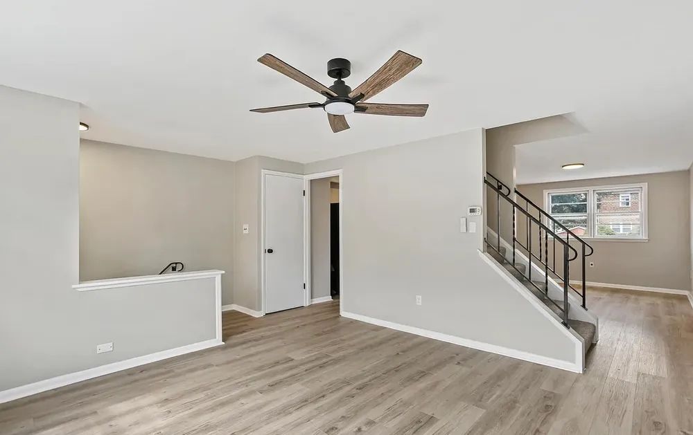 Living room with gray walls, wood floors, stairs, and ceiling fan.