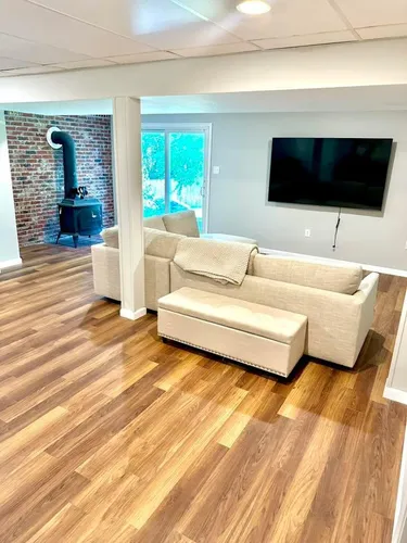 Living room with wood floors, sectional sofa, TV, brick wall with stove, and sliding glass door.
