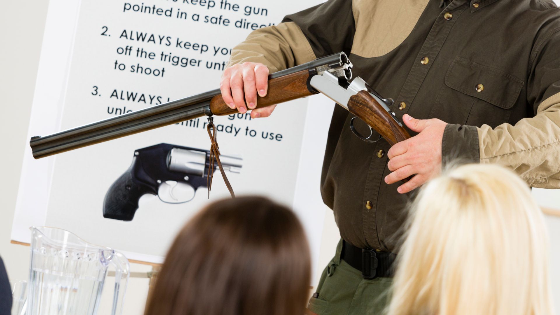 Man demonstrating firearm safety rules with a shotgun, in front of a group.