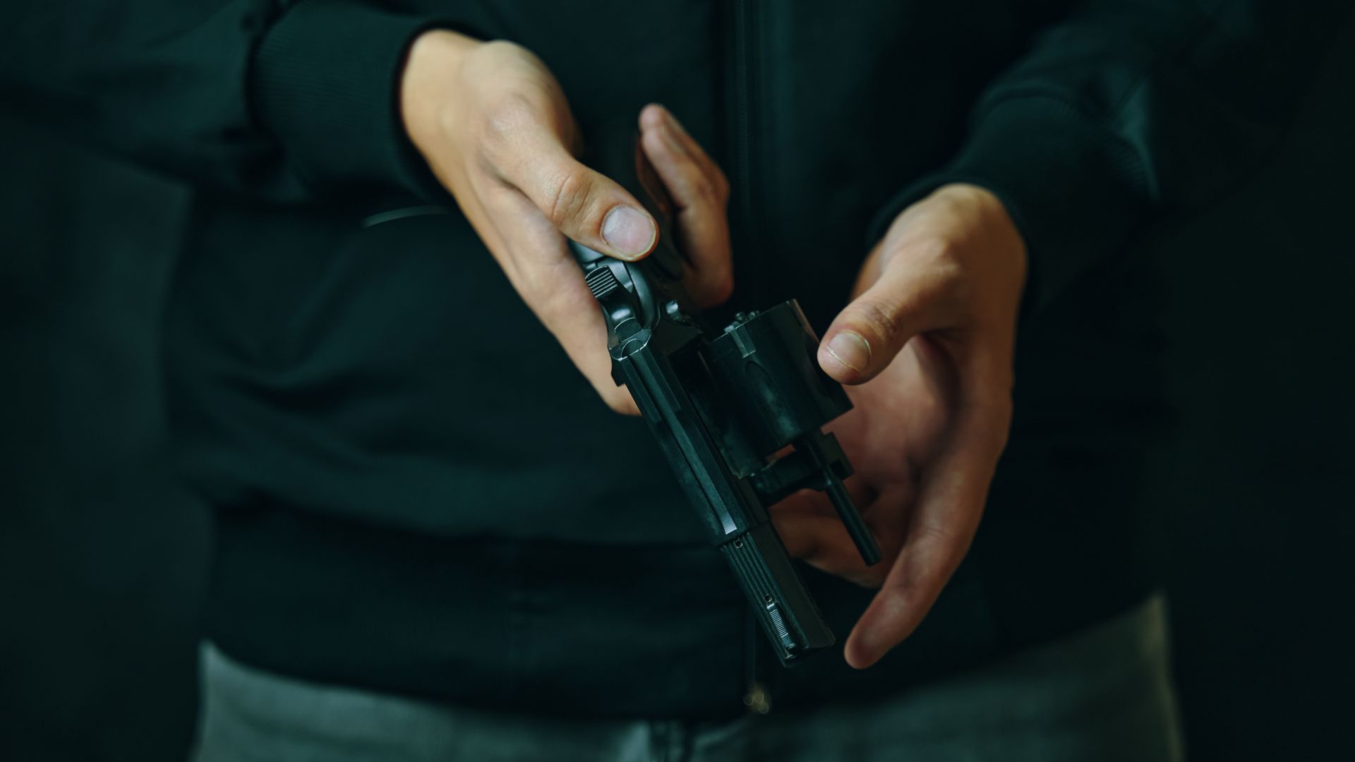 Person holding a revolver, opening the cylinder. Dark background.