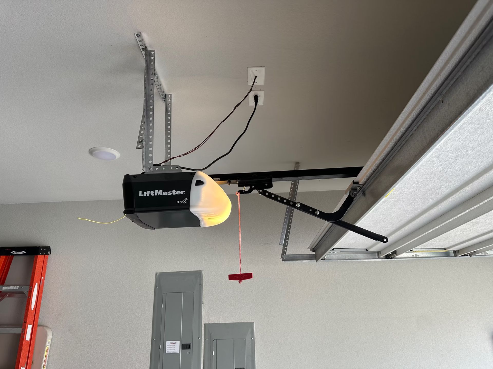 Garage ceiling with an electric garage door opener, power outlet, and partially open garage door.