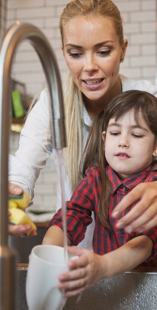 Woman and child washing a cup in the kitchen sink. The woman is blonde, child has brown hair.