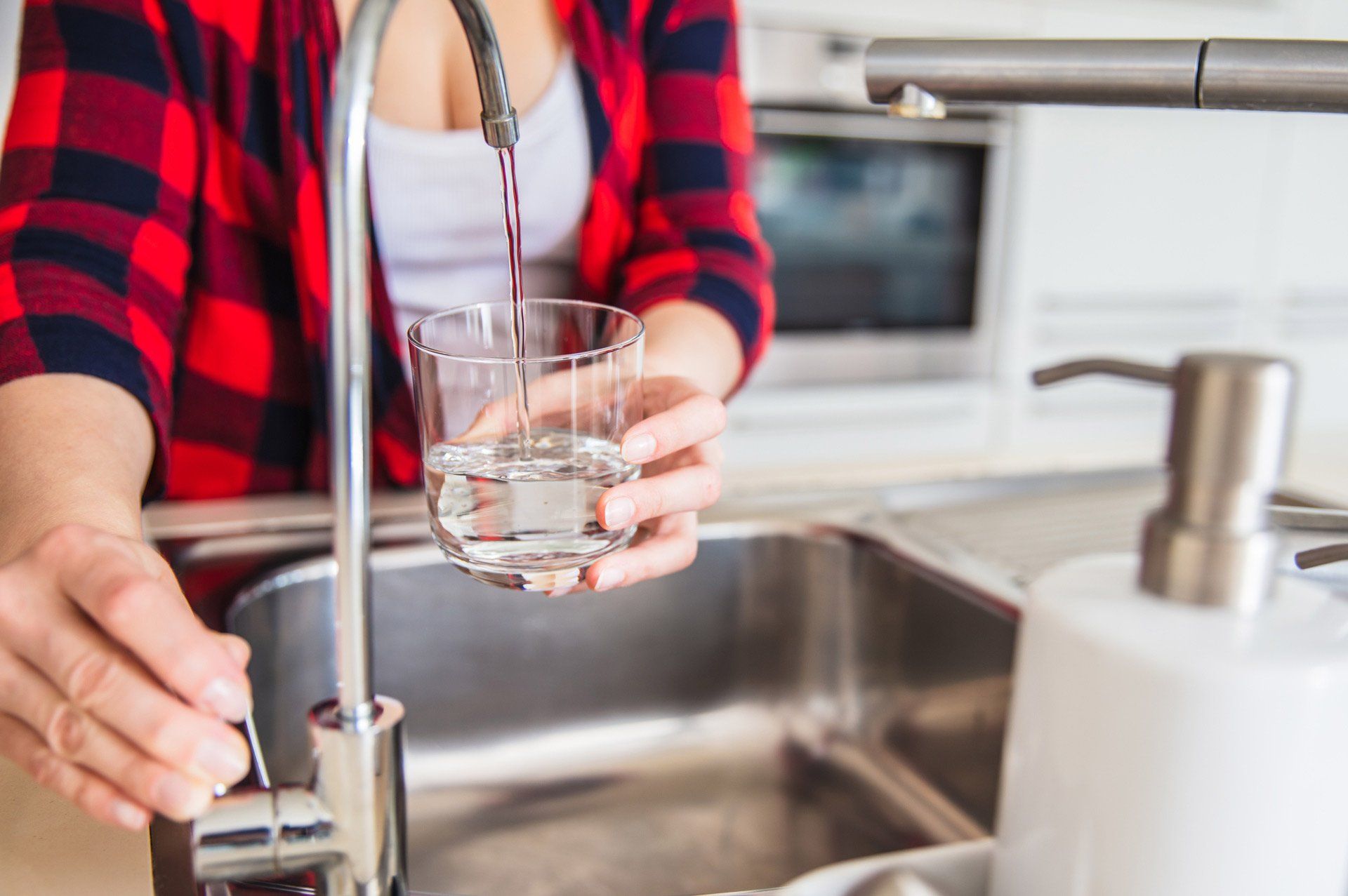 Woman filling a glass with water at a kitchen sink.