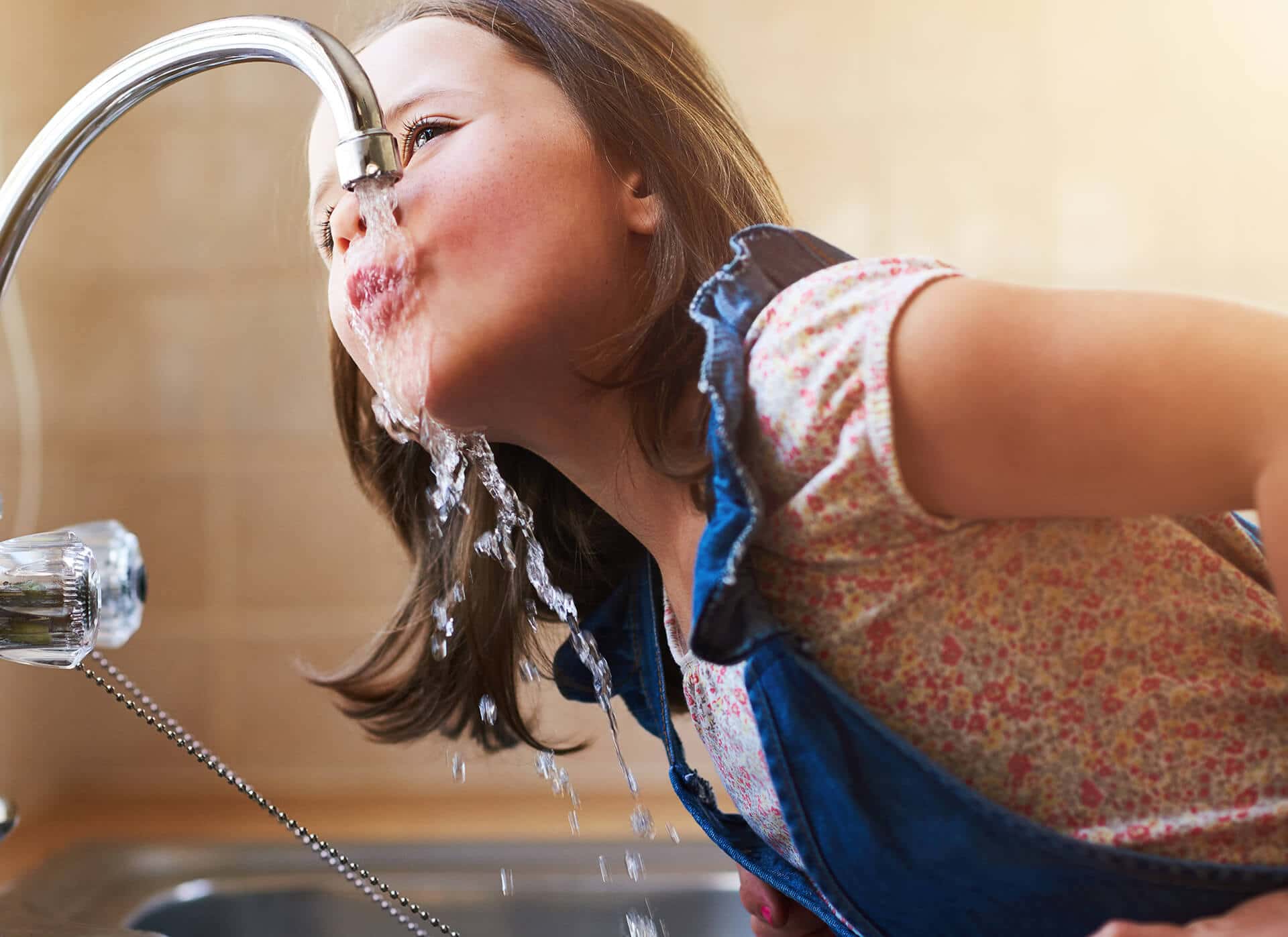 Girl drinking water from a kitchen faucet.
