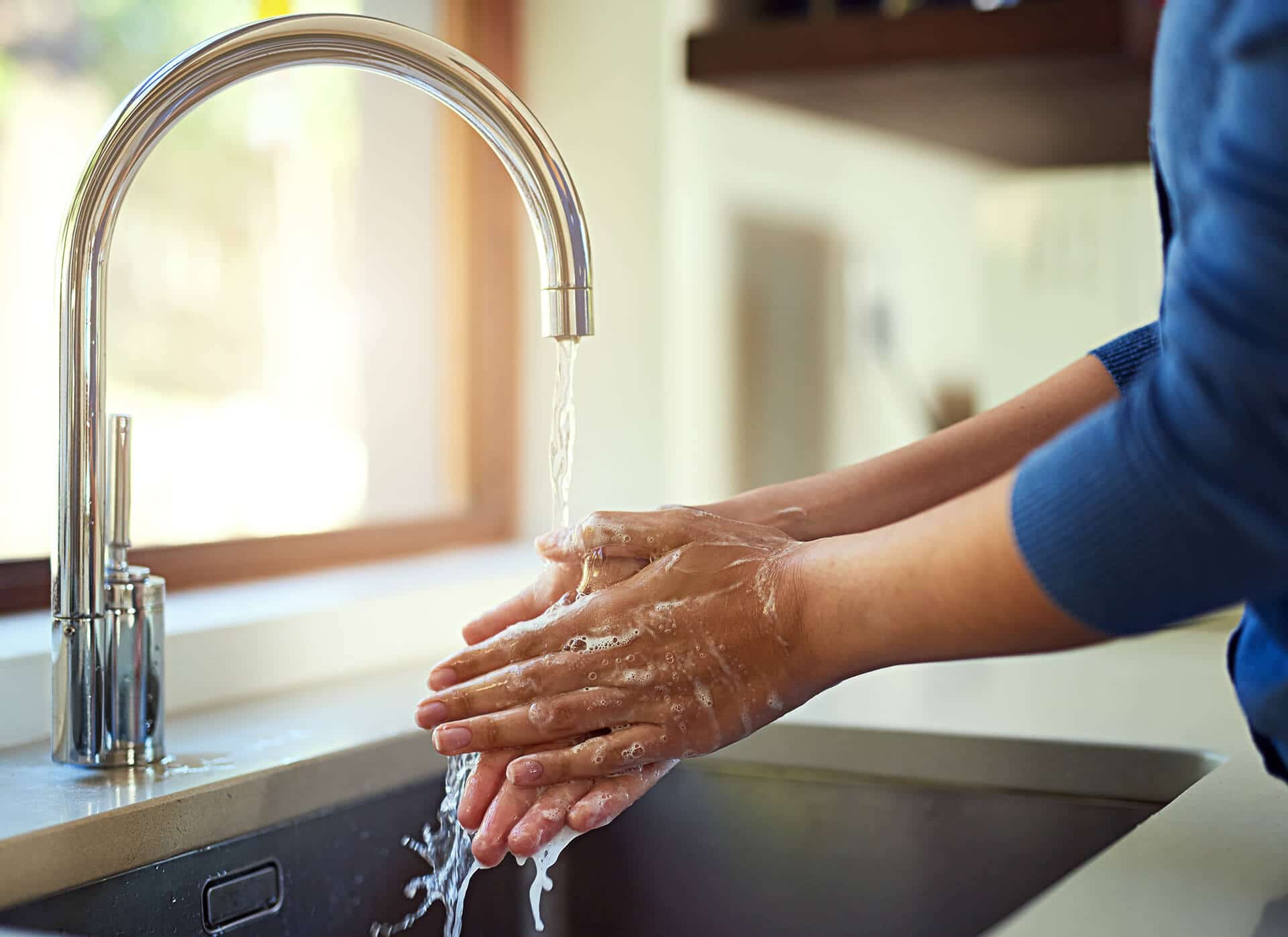 Person washing hands with soap under a chrome faucet in a kitchen sink.
