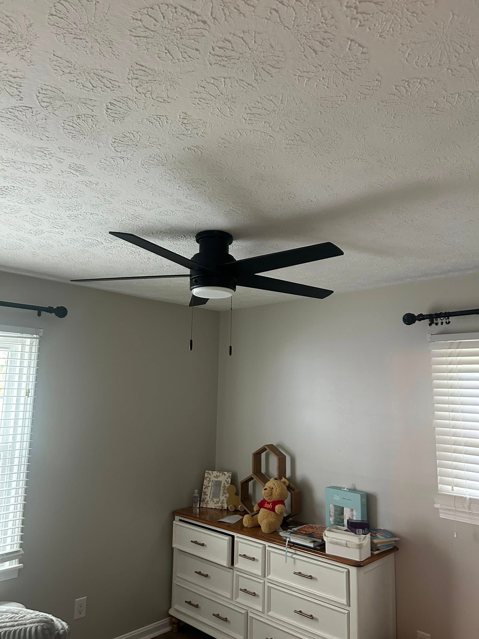 Black ceiling fan in a bedroom with a white dresser and window.