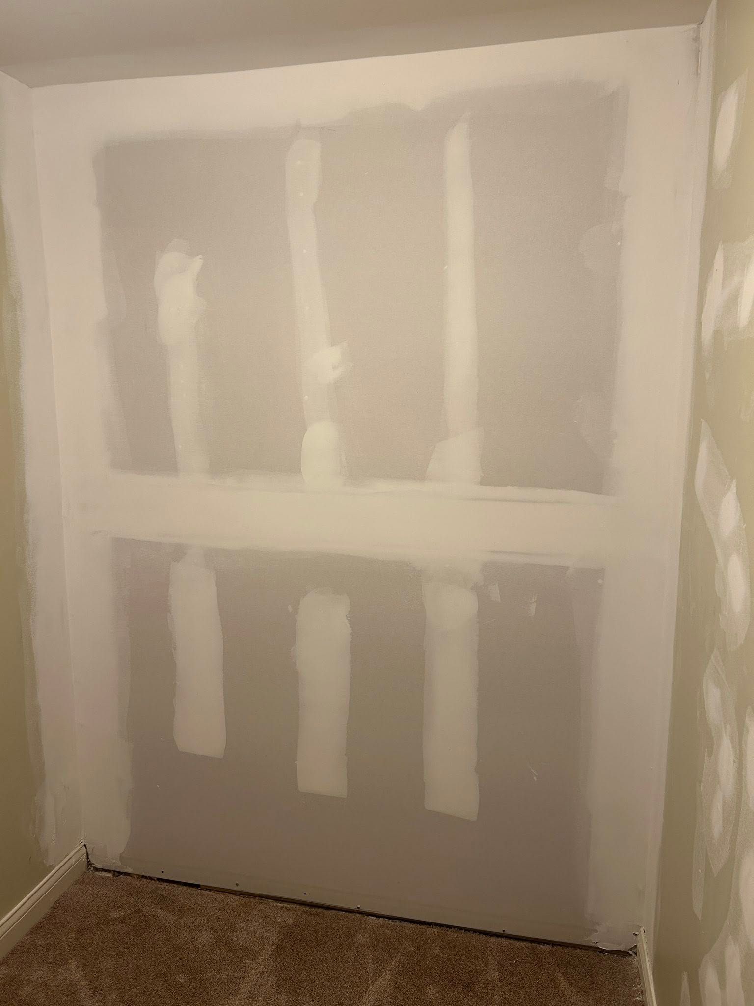 Drywall partially installed in an alcove with visible seams, white mud, and carpeted floor.