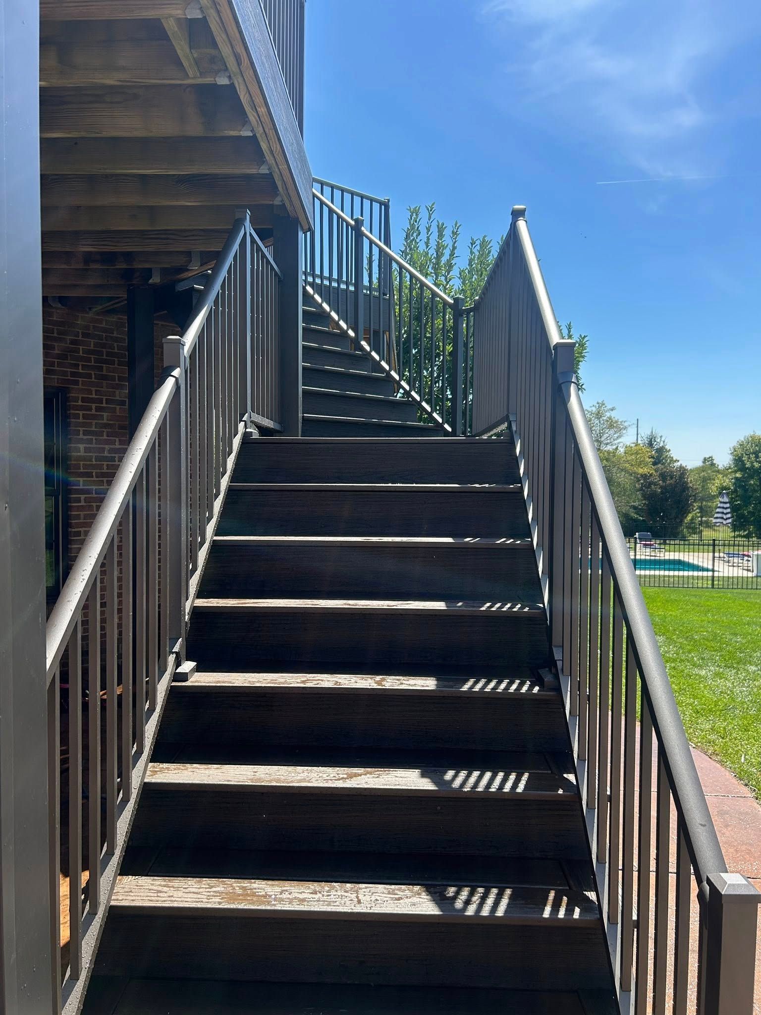 Exterior wooden staircase with metal railings leading upwards to an upper level, sunny day.