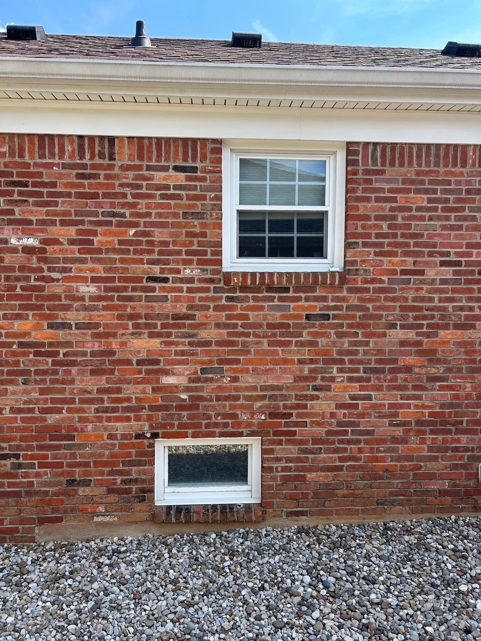 Red brick building with two white-framed windows, against a blue sky.
