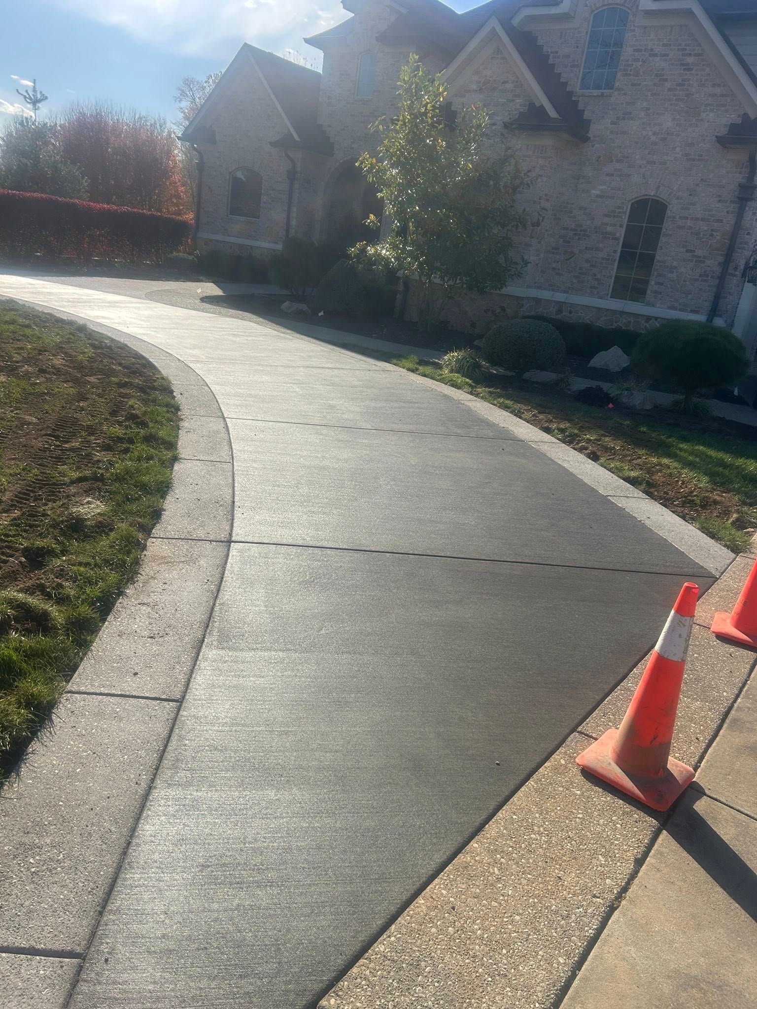Driveway with orange cones, leading to a large house with a stone facade, and landscaping.